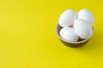 Chicken eggs in bowl on yellow background with copy space