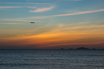 Colorful dawn, sunset on a calm sea, sunrise. Beautiful sea background. A charming start to the day.  Silhouette of an airplane ready for landing, amid the dawn.