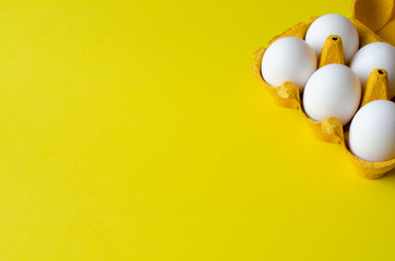 Chicken eggs in tray on yellow background with copy space