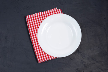 Empty white plate and red napkin on black table.