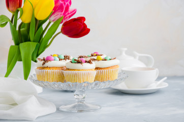 Homemade Easter vanilla cupcakes bird's nest with butter cream, chocolate and candy eggs on a dish. Easter fun food idea for kids. Horizontal orientation. Copy space.