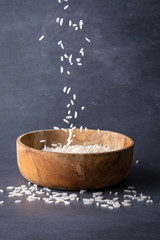 Close-up of white rice levitating on wooden bowl on gray background, vertically with copy space