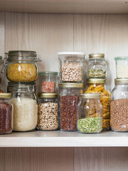 Shelf in the kitchen with various cereals and seeds - peas split, sunflower and pumpkin seeds, beans, rice, pasta, oatmeal, couscous, lentils, bulgur in glass jars