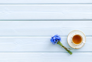 Summer tea party. Cup near cornflowers bouquet on blue wooden background top-down copy space