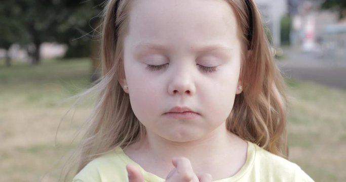 Stock video of a lovely thoughtful child picking her nose in the street. Unfocused blurred background in the park.
