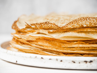Stack Russian homemade thin pancakes on white plate on wood background. Traditional wheat pancakes for Shrovetide.