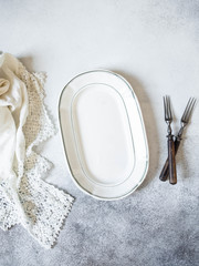 Vintage table setting with oval plate, white lace napkin and forks on a grey background. Top view. Copy space