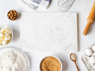 Frame of various baking ingredients - flour, eggs, sugar, butter, dry yeast, nuts and nuts, kitchen utensils and white marble board. Top view.