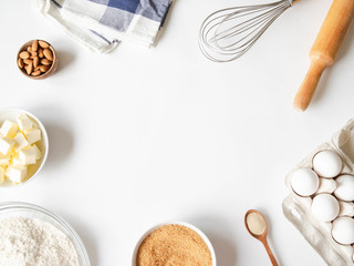 Frame of various baking ingredients - flour, eggs, sugar, butter, dry yeast, nuts and kitchen utensils on white background. Top view.