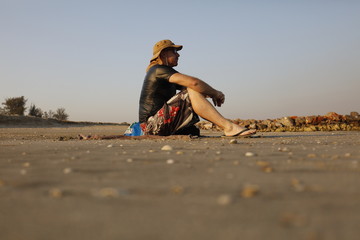 A caucasian man with a flat hat sits on the beach