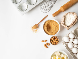 Fototapeta na wymiar Set of various baking ingredients - flour, eggs, sugar, butter, nuts, kitchen utensils and cupcake baking dish on white background. Top view.