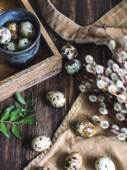 Easter composition with eggs in blue cup on wood tray with willows and leaves on a dark wood background.