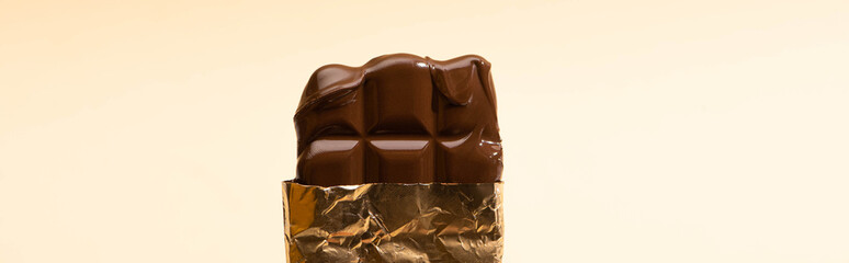 delicious milk chocolate bar in golden foil isolated on beige, panoramic shot