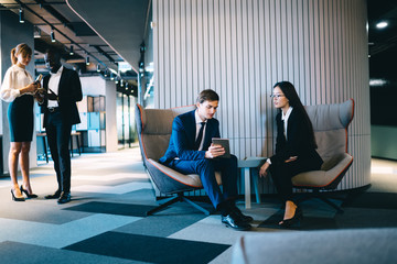 Multiethnic office employees in formal wear browsing gadgets at lobby of business center