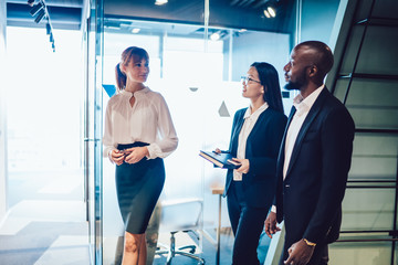 Multiethnic business partners communicating while stepping after female secretary to office