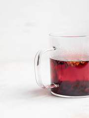Glass transparent mug with purple hot hibiscus tea with slices of various dried fruits and berries...