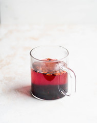 Glass transparent mug with purple hot hibiscus tea with slices of various dried fruits and berries isolated lifestyle photo