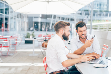 Two beautiful young businessmen sitting bar using computer and smartphone