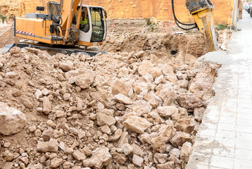 Excavator crushing rocks to start construction of houses in a town in Spain.