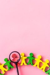 Wooden figures of people under black magnifying glass on pink table. Recruitment, hiring, leadership concept.