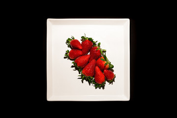 bouquet of red strawberries on a white plate with a black background