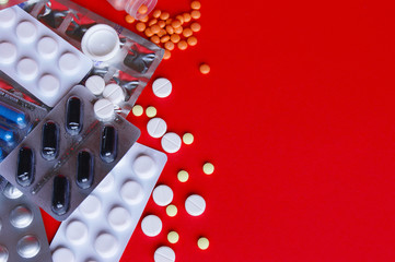 Assorted pharmaceutical medicine pills, tablets and capsules on red background