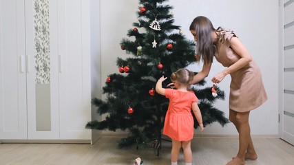 happy mother and little daughter decorating christmas tree at home. concept family, winter holidays and people.