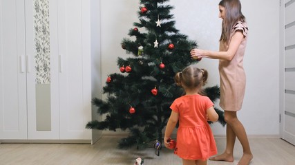 Merry Christmas and Happy Holidays. Mom and daughter decorate the Christmas tree indoors. The morning before Xmas. 