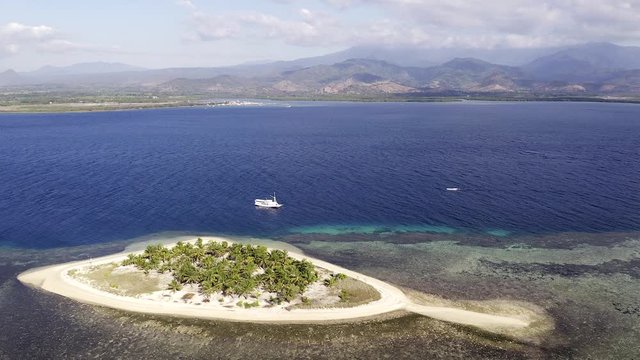 Tourist boat anchored next to Pulau Bedil, a tiny Indonesian beautiful island off the coat of Lombok, Aerial view.