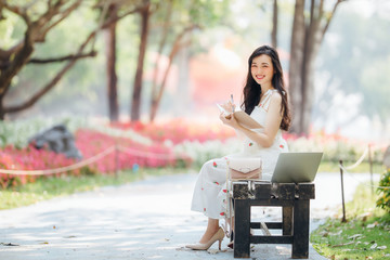 Asia beautiful woman sitting on black chair and working receive orders from internet in garden.