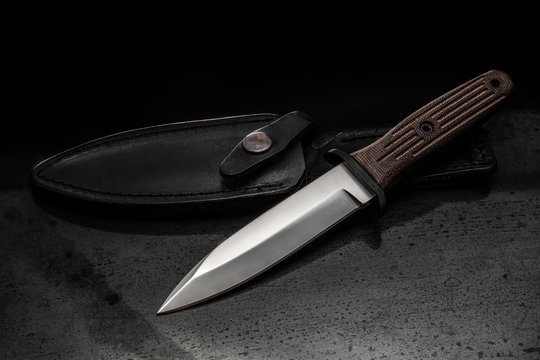 A modern hunting knife and a leather case for him on a dark background. Melee weapons for hunting and self-defense. The instrument of crime.