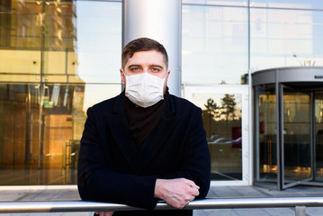 Handsome Caucasian young man near his office wearing surgical face mask during global coronavirus...