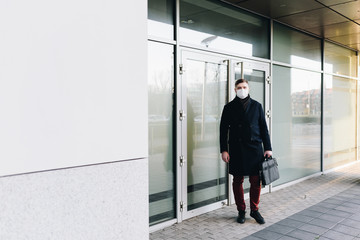 Young Caucasian man leaving his office wearing surgical face mask to protect from coronavirus covid-19 virus