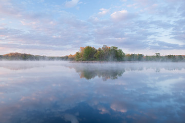 Fototapeta na wymiar Landscape at sunrise of the foggy, spring shoreline of Whitford Lake with reflections in calm water, Fort Custer State Park, Michigan, USA