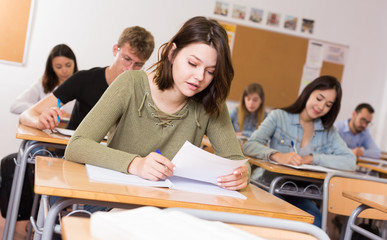 Obraz premium Smiling schoolgirl is learning and answering the question on paper