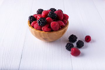 moras i frambuesas en un cuenco de madera sobre una mesa rústica blanca