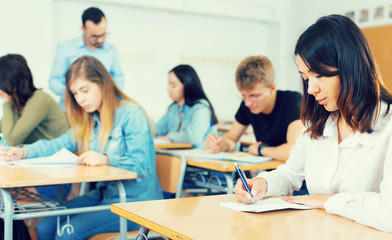 Fototapeta premium Young girl is writing test and thinking about questions at the desk