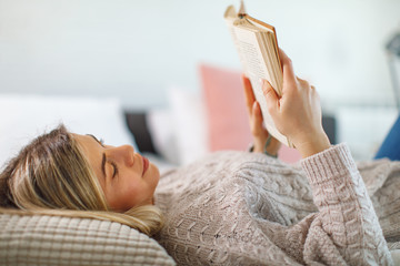 Young woman lies on her back in bed reading a book