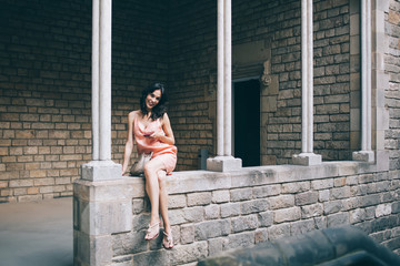 Graceful woman sitting with crossed legs on stone wall with smartphone