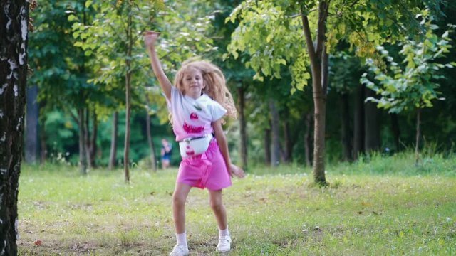 Little kid dancing in green park. Outdoor portrait of happy girl in park