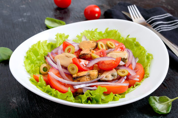 Salad of marinated mussels, fresh tomatoes, red onions, olives in a bowl on a black background