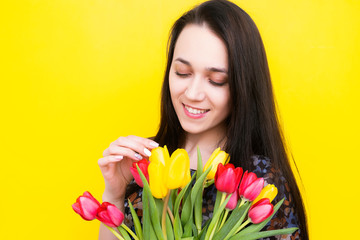 Brunette with a bouquet of tulips on a yellow background. Young woman with flowers. Women's Day.