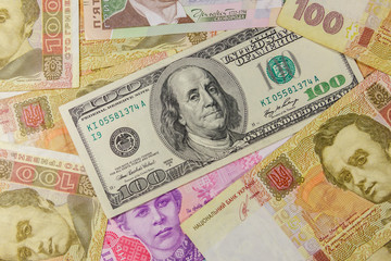 Fototapeta na wymiar One hundred dollar bill on a background of different ukrainian hryvnia banknotes