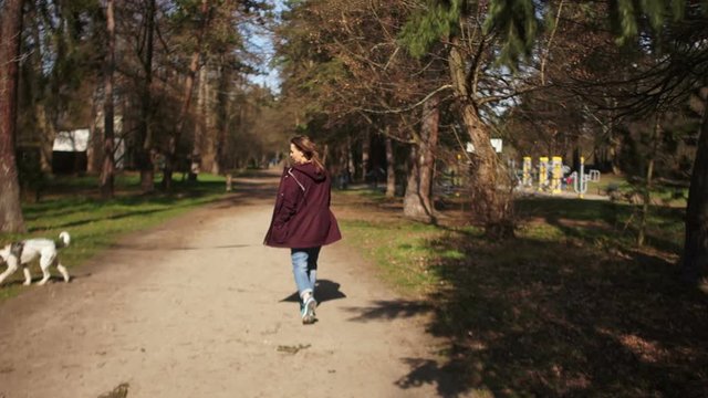 Beautiful girl with a backpack on her back walks her dog on a leash in the spring park. Dog walk, village life, pet care, happy weekend