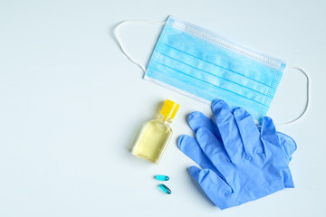 Hand sanitizer gel bottle, face mask, rubber gloves, pills on blue background. Coronavirus Disease...