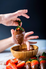 manos de una ni&ntilde;a cogiendo  una fresa y untanda en chocolate