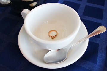 Wedding golden engagement ring in white cup for tea, marriage proposal. Love and wedding concept. Beautiful stylish golden ring with a diamond.