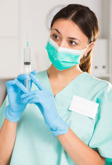 Female nurse in mask holding syringe for injection in hospital