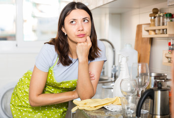 Tired girl housewife in apron holding gloves at  kitchen