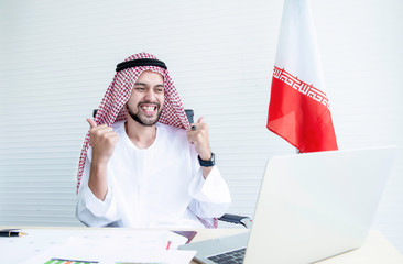 Iranian businessman receiving good news on laptop with fists raised and Iranian flags